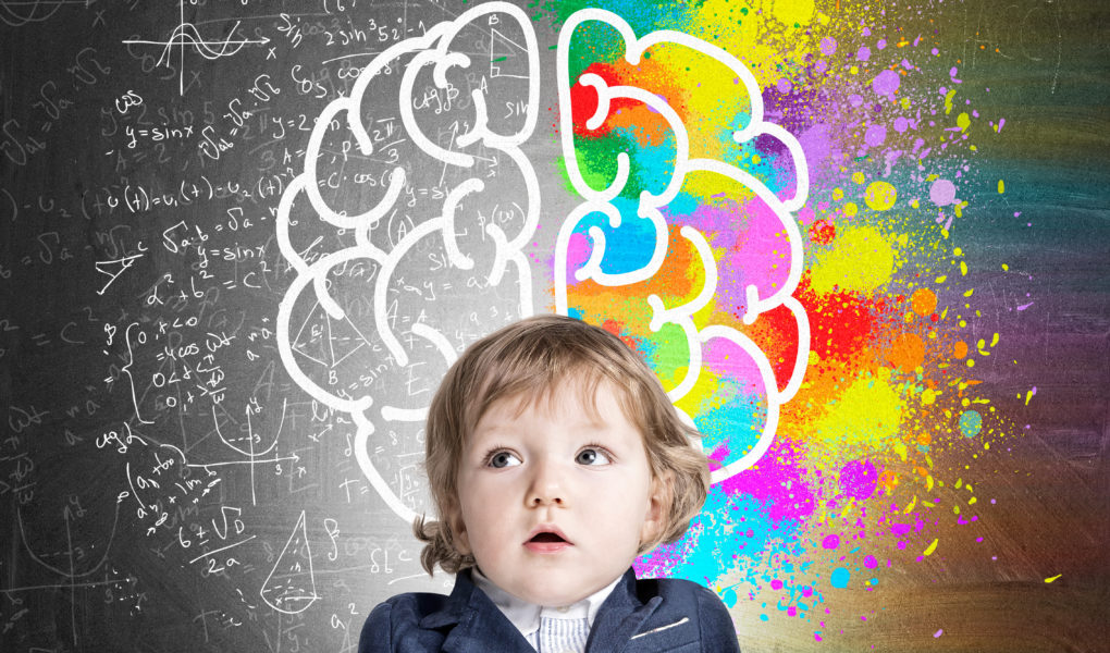 Portrait of an adorable little boy wearing a suit and standing near a chalkboard with a colorful brain sketch. Concept of child's development